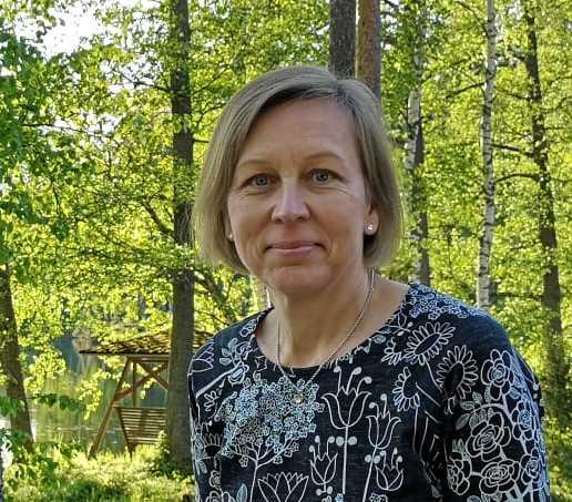 Jyväskylän seurakunnan uusi hautaustoinen päällikköTuija Pajunen ulkona takanaan vehreä metsämaisema.