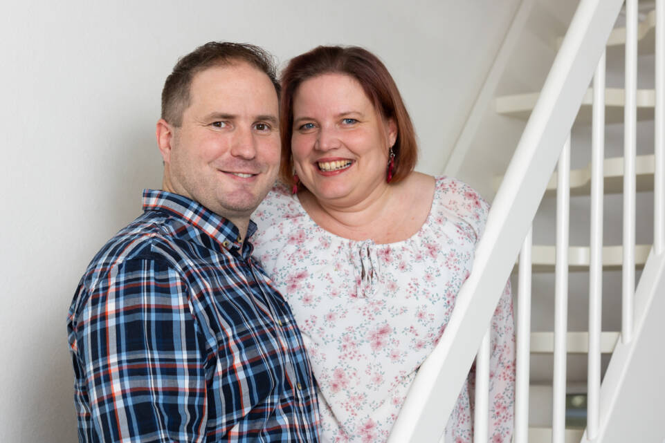 Mikko ja Liisa hymyilevät kameralle, taustalla valkoinen portaikko.