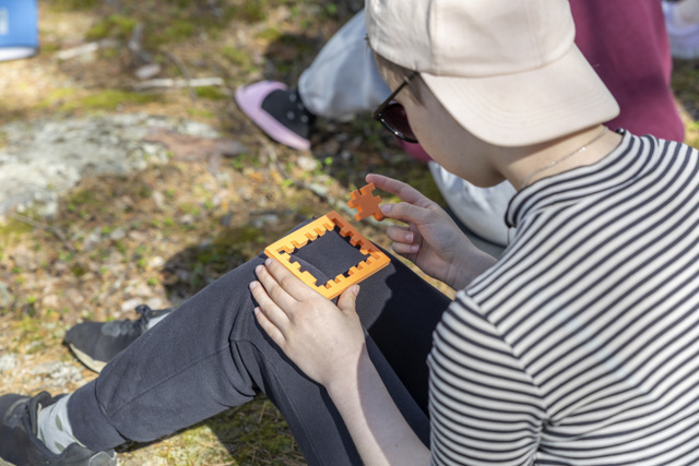 Rippikoululainen kokoaa pientä palapeliä lippis päässä.