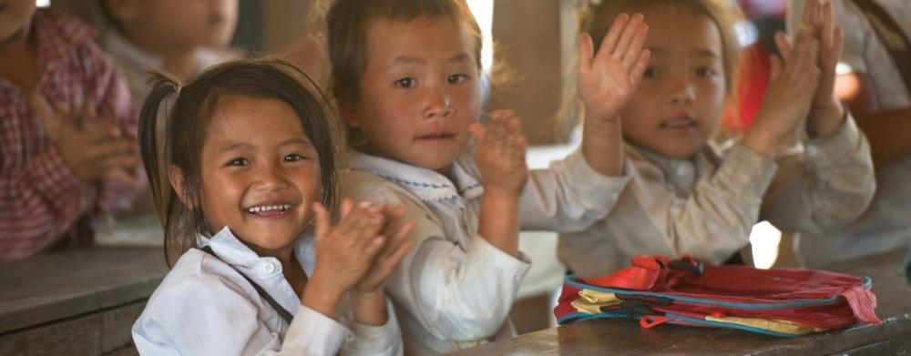 Laoslaisia tyttöjä koulunpenkillä hymyilevät ja taputtavat