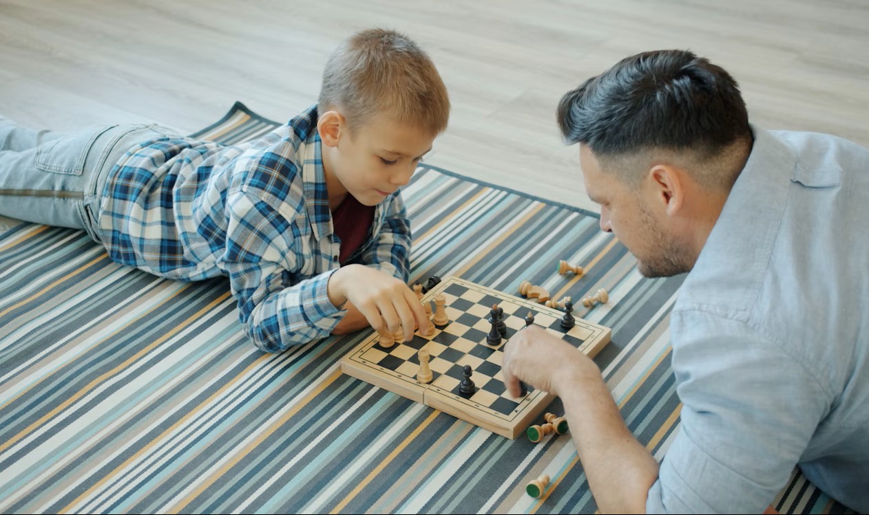 Mies ja lapsi pelaavat shakki lattialla