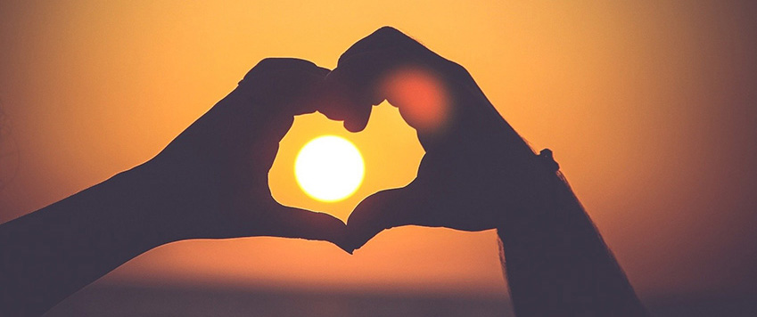Auringonlasku käsistä muodostetun sydämen läpi kuvattuna.