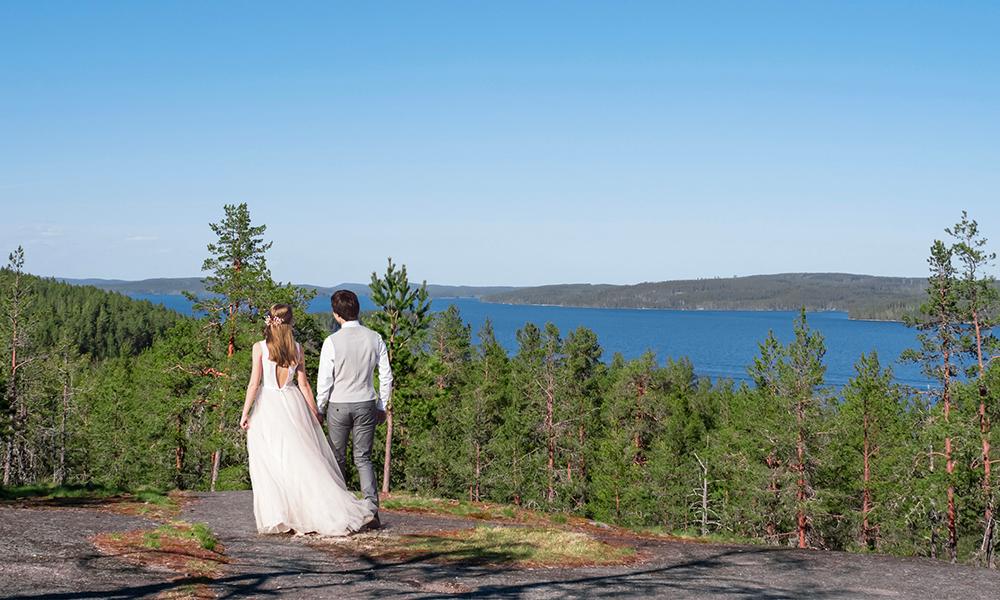 Vihkipari kalliolla, sininen taivas ja metsä